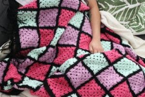 girl sitting with a colorful granny square blanket on her