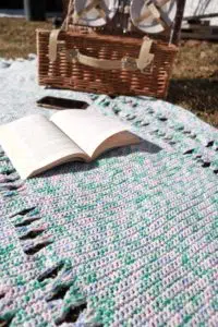 crochet picnic blanket on the ground with a book opened on top of it