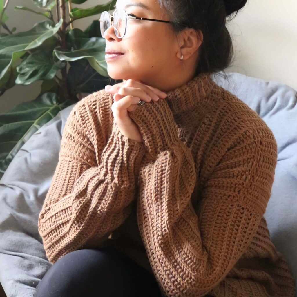 girl sitting on a chair wearing an easy crochet sweater pattern